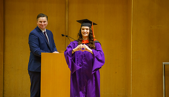 A graduate makes a heart with their hands before walking across the stage.